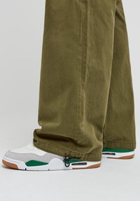 Białe i szare sneakersy z zielonymi akcentami oraz poduszką powietrzną, zestawione z oliwkowymi spodniami w luźnym kroju z prostą nogawką.