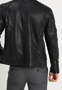 Svart lädermotorcykeljacka med texturerade axlar och sidopaneler. Har dragkedjeslutningar i ärmarna och perforerad detaljer på baksidan.