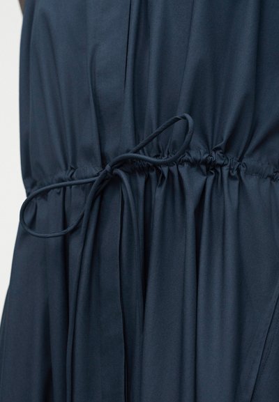 Σκούρο μπλε ύφασμα με ζωνάρι στη μέση, σούρωμα, δεμένο με λεπτό κορδόνι στον ίδιο χρωματισμό σε φιόγκο.