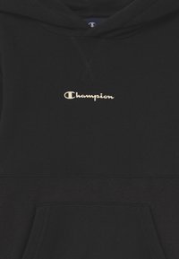 Felpa con cappuccio nera, dal morbido tessuto in pile, con un grande logo bianco "Champion" sul davanti e una tasca a marsupio.
