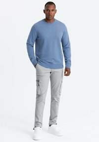 Světle modrý svetr s kulatým výstřihem z měkké tkaniny; spárovaný se světle šedými cargo kalhotami s kapsami na zip a bílými teniskami.