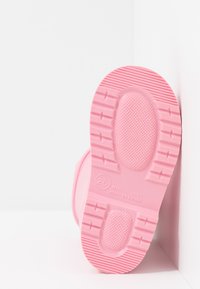 Suela de zapato de goma rosa con superficie texturizada, que presenta un patrón circular y surcos. Marcada con "25" y "HECHO EN ESPAÑA."