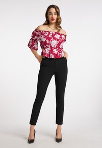 Rød blomsteret off-the-shoulder top med flæser på ærmerne, indsnævret talje, parret med skræddersyede sorte bukser og sorte højhælede sko.