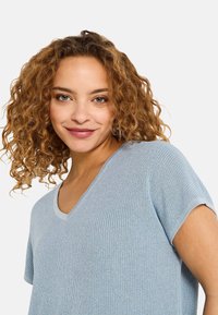Top de punto azul claro con escote en V, mangas cortas y una tela texturizada. Presenta un corte holgado y acabados acanalados en el escote y las mangas.
