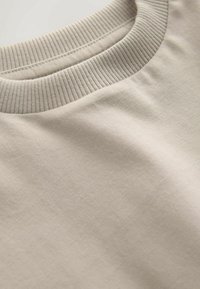 Hellbeiges Sweatshirt mit Rundhalsausschnitt aus weicher Baumwolle, mit geripptem Kragen, das eine glatte Textur und zurückhaltende Designdetails zeigt.