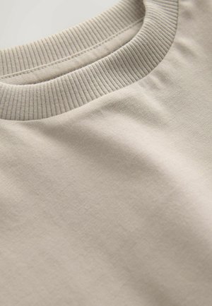 Hellbeiges Sweatshirt mit Rundhalsausschnitt aus weicher Baumwolle, mit geripptem Kragen, das eine glatte Textur und zurückhaltende Designdetails zeigt.