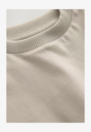 Valge beež tooni pehme puuvillane ümbertõmmatud kaelusega pusapluus, millel on soonikrae ning sile tekstuur ja tagasihoidlik disain.