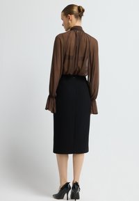 Braune durchsichtige Bluse mit gerafften Bündchen, kombiniert mit einem schwarzen Bleistiftrock. Schwarze hochhackige Schuhe vervollständigen das Outfit. Klare Linien und elegante Passform.