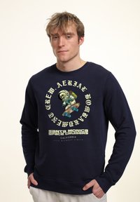 Sudadera azul marino de manga larga, con un gráfico de un esqueleto en un traje de astronauta sobre una patineta. El texto incluye "Santa Monica Space Cruisers."