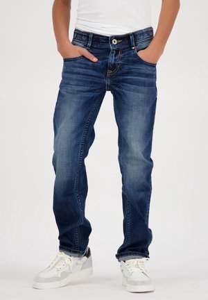 Vaqueros de mezclilla azul oscuro con un lavado desgastado, corte recto, bolsillos delanteros y detalles cosidos. Combinados con zapatillas blancas.