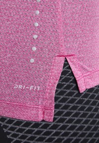 Camiseta deportiva rosa Dri-FIT con un patrón texturizado, detalles de botones y aberturas laterales, combinada con leggings negros con estampado.