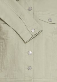 Světle béžová džínová bunda s kovovými knoflíky na cvoky, viditelnou náprsní kapsou s klopou a detailním šitím na rukávu a těle.