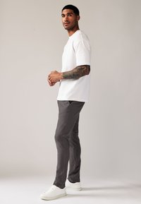 Biała bawełniana koszulka z krótkim rękawem w połączeniu z szarymi, dopasowanymi spodniami oraz białymi trampkami, charakteryzująca się gładką fakturą i subtelnymi detalami przeszyć.