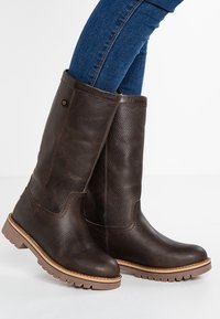 Stivali al ginocchio in pelle marrone con finitura testurizzata, punta rotonda, suola in gomma e dettagli di cucitura discreti. Adatti a diverse condizioni atmosferiche.