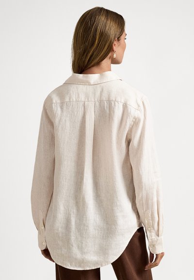 Light beige long-sleeve linen shirt with a pointed collar, rounded hem, and button cuffs, displaying a relaxed fit and textured fabric.