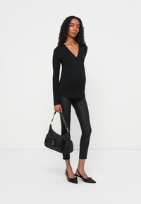 Zwart langemouwen top met een V-hals, strakke zwarte nepleer legging, zwarte handtas met gouden accenten en zwarte puntige ballerina's.