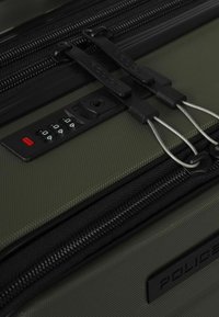 Valigia verde testurizzata con cerniere nere e una serratura combinata nera integrata che blocca due cursori delle cerniere con cavi metallici.