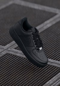 Sapatilha Nike Air Force 1 preta em pele com uma superfície texturizada, biqueira arredondada, atacadores pretos planos e etiqueta prateada na língua.