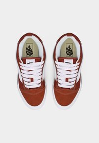 Paire de baskets Vans orange rouille et blanches avec des lacets blancs vues de dessus sur un fond blanc uni.