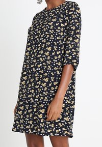 Kwiatowa sukienka w czarnym kolorze o luźnym kroju, z żółtymi i białymi kwiatami, trzyczwartowymi rękawami i okrągłym dekoltem. Gładka tekstura.