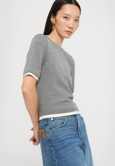 Gray short-sleeve sweater with textured dots, cream trim at neck and hem, paired with light blue high-waisted jeans.