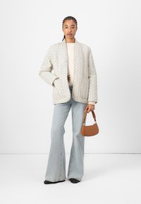 Chaqueta acolchada y estampada en color blanco roto con un corte relajado, combinada con pantalones de mezclilla acampanados en azul claro y un pequeño bolso marrón.
