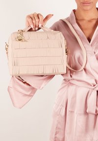 Jasnoróżowa torebka wykonana z teksturowanego materiału, z frędzlami, uchwytem u góry, odczepianym paskiem na ramię i złotymi akcentami.