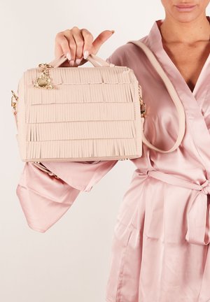 Lichtroze handtas van gestructureerd materiaal, met een franjesontwerp, bovenhandgreep, afneembare schouderriem en gouden hardware accenten.