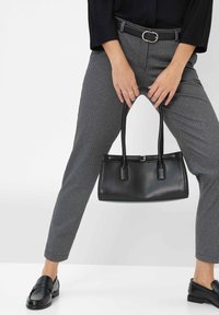 Schwarze Lederhandtasche mit zwei Griffen, rechteckiger Form, glatter Textur. Kombiniert mit grauen Hahnentritt-Hosen und schwarzen Loafers.