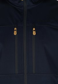 Marine softshell jakke med sorte lynlåse og brune læderhåndtag, med to frontlynlås lommer og en høj krave for ekstra varme.