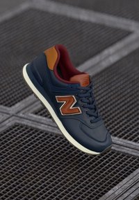 Navy leather sneaker with brown accents, featuring a white rubber sole and a prominent 'N' logo. Textured surface and padded collar.