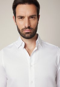 Biała koszula na guziki z usztywnianym kołnierzem, gładkiej bawełnianej tkaniny o subtelnej fakturze. Posiada standardowy krój i przejrzyste plastikowe guziki.