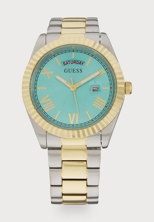 Strieborné a zlaté kovové hodiniek s tyrkysovým ciferníkom. Obsahuje zúbkovaný rám, rímske číslice, zobrazenie dátumu a indikátor soboty.