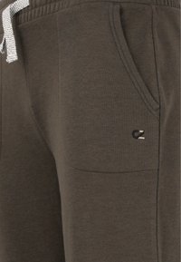 Dark brown sweatpants made of soft fabric, featuring a drawstring waist, side pocket, and a small logo detail.