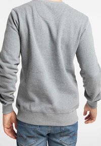 Felpa grigia con una texture morbida, collo rotondo e polsini a costine. Dettaglio di cucitura notevole sul retro, abbinata a pantaloni jeans blu.