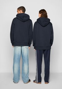 Mørkeblå hettegensere med avslappet passform, som har store hetter og ribbede mansjetter, sammen med lyseblå vide jeans og mørke treningsbukser.