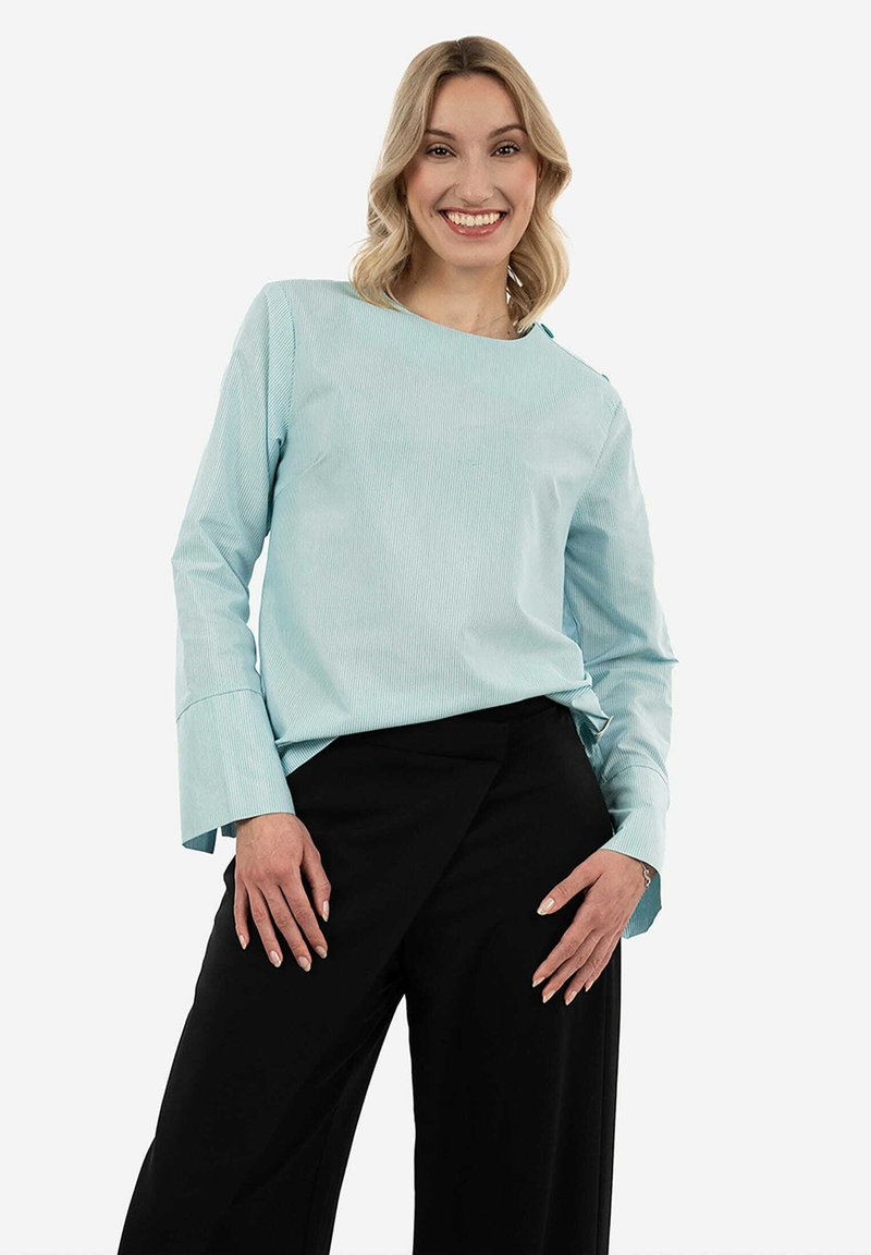 Top azzurro chiaro a maniche lunghe con finitura testurizzata, scollatura rotonda e ampi polsini, abbinato a pantaloni neri a gamba larga. Design semplice.