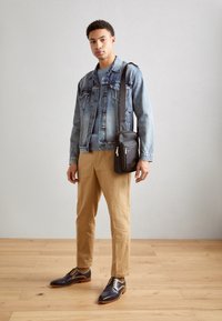 Giacca di jeans, maglione azzurro chiaro, pantaloni beige e scarpe marrone scuro con dettagli beige. Borsa a tracolla nera con cerniere argentate.