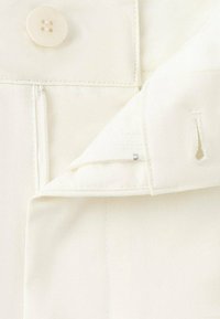 White fabric with a smooth texture, featuring a button closure and a zipper on the left side, with stitching details and a minimal design.