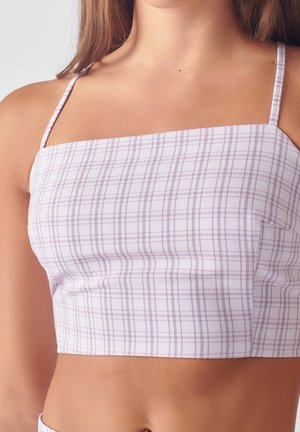 Femme portant un crop top ajusté, sans manches, avec de fines bretelles et un motif à carreaux violet clair, visible des épaules jusqu'au milieu du ventre.