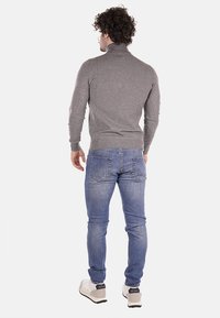 Pullover grigio a collo alto con un design aderente, abbinato a jeans azzurri. L'outfit include scarpe da ginnastica e dettagli di cucitura visibili.