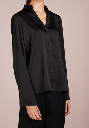 Blouse en satin noir avec un col pointu, des manches longues, une fermeture à boutons sur le devant et une coupe décontractée. Texture lisse et design minimaliste.