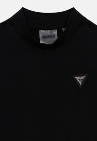 Μαύρο κοντομάνικο μπλουζάκι με ψηλό λαιμόκοψη, διακοσμημένο με τρίγωνο κονκάρδα με ασημί λεπτομέρειες στο στήθος. Απαλή υφή υφάσματος.