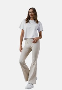 Biała krótka koszulka w połączeniu z jasnobeżowymi spodniami typu dzwony. Stylizacja charakteryzuje się gładką fakturą i swobodnym fasonem, uzupełniona białymi sneakersami.