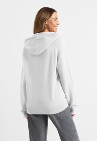 Lichtgrijze hoodie met geribde zoom en manchetten, met een losse pasvorm en een soepele textuur. Gemaakt boven een donkergrijze broek.