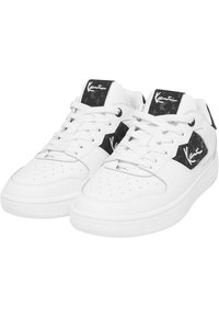 Fehér sportcipők sima bőr felsőrésszel, fekete részletekkel a nyelvén és az oldalán, perforált orrrésszel és lapos fűzőkkel.