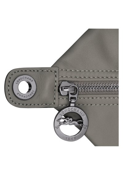 Graues Lederetui mit silbernem Reißverschluss, ausgestattet mit einem runden Anhänger mit eingeprägtem Logo und einer laufenden Figur sowie genähten Details an den Kanten.