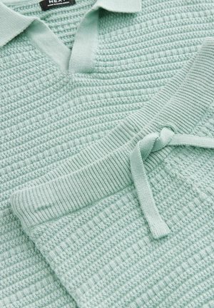Lichtgroene gebreide polo trui met een textuurpatroon en een V-hals. Vergezeld van bijpassende broek met een tailleband en een strikdetail aan de voorkant.
