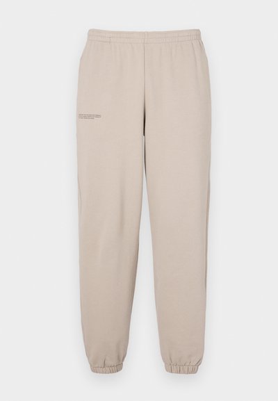 Beige sweatpants lavet af blødt stof, med elastisk talje og manchetter, samt en lille trykt tekstdetalje på venstre ben.