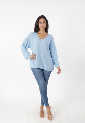 Suéter de punto azul claro con escote en V y mangas holgadas, combinado con jeans ajustados azules y sandalias de tacón transparente.